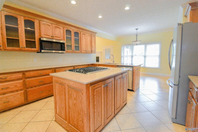 kitchen with hanging light fixtures, sink, ornamental molding, stainless steel appliances, and a center island