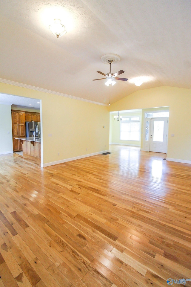 unfurnished living room with light hardwood / wood-style flooring, lofted ceiling, a textured ceiling, and ceiling fan with notable chandelier