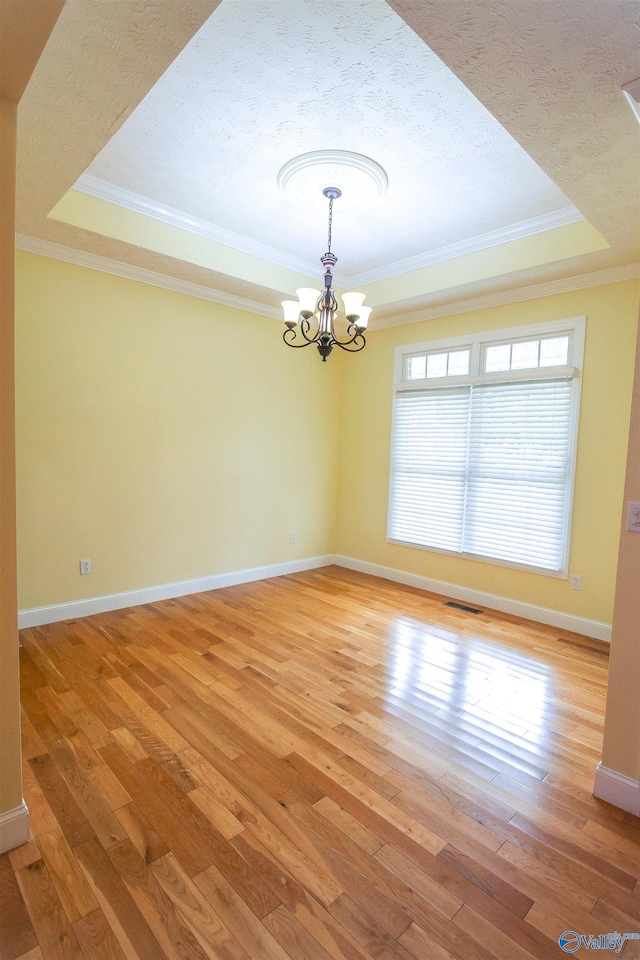 spare room featuring a raised ceiling, light hardwood / wood-style floors, ornamental molding, and a notable chandelier