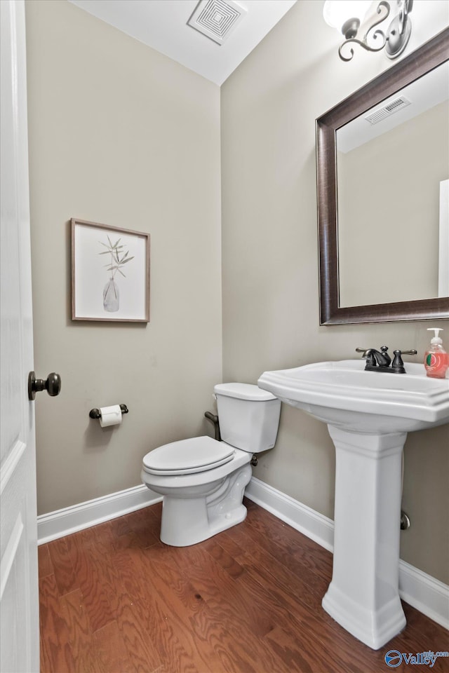 half bath with toilet, visible vents, and wood finished floors