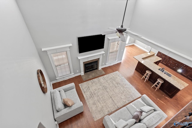 living room featuring baseboards, a ceiling fan, a towering ceiling, wood finished floors, and a fireplace