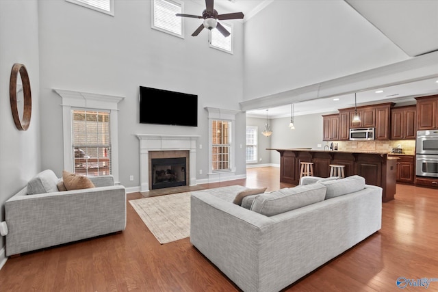 living area with ceiling fan, a tile fireplace, wood finished floors, baseboards, and ornamental molding