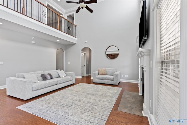 living area with arched walkways, ornamental molding, ceiling fan, wood finished floors, and baseboards