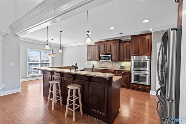 kitchen with crown molding, backsplash, appliances with stainless steel finishes, wood finished floors, and a kitchen breakfast bar