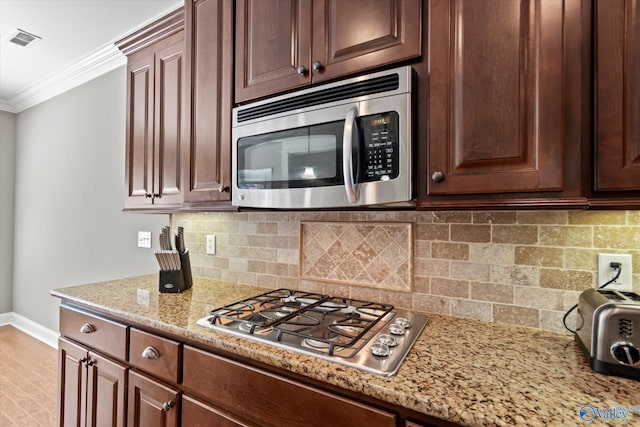 kitchen with visible vents, ornamental molding, appliances with stainless steel finishes, decorative backsplash, and light stone countertops