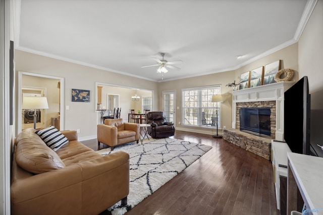 living room with ceiling fan with notable chandelier, a fireplace, crown molding, baseboards, and dark wood-style flooring