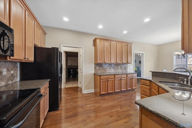 kitchen featuring tasteful backsplash, recessed lighting, wood finished floors, black appliances, and a sink