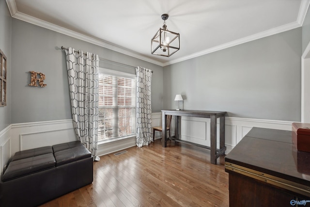 sitting room featuring a notable chandelier, ornamental molding, a wainscoted wall, and wood finished floors