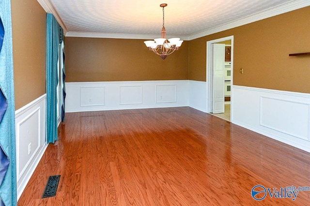 spare room featuring wainscoting, visible vents, a chandelier, and ornamental molding