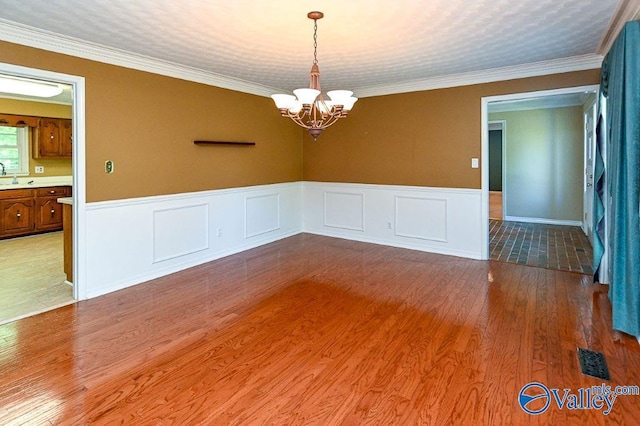 spare room with a wainscoted wall, a sink, visible vents, a notable chandelier, and wood finished floors