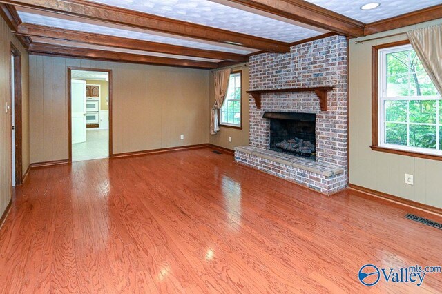 unfurnished living room featuring wood finished floors, visible vents, beam ceiling, baseboards, and a fireplace