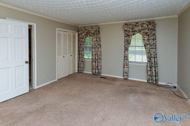 unfurnished bedroom featuring carpet flooring, visible vents, baseboards, a closet, and crown molding