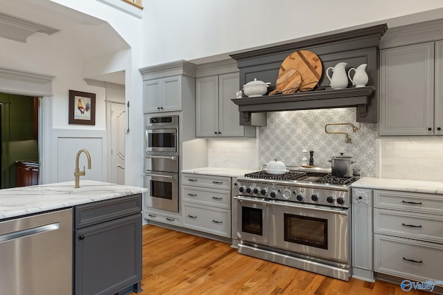 kitchen featuring appliances with stainless steel finishes, tasteful backsplash, gray cabinetry, light stone counters, and light hardwood / wood-style floors