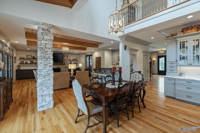 dining room with light hardwood / wood-style floors, an inviting chandelier, ornate columns, and a stone fireplace