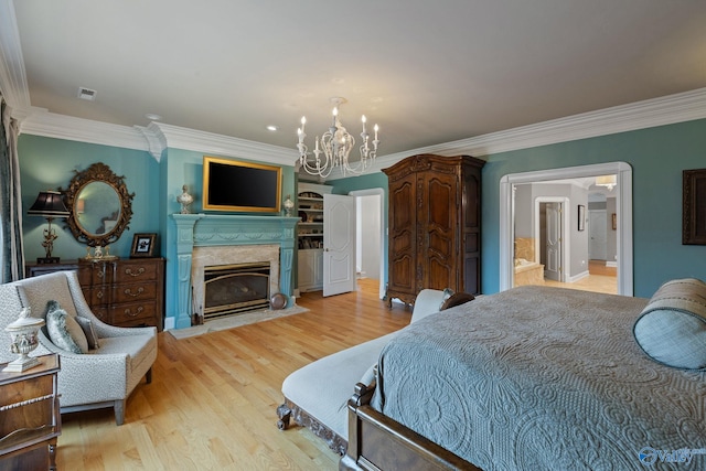 bedroom featuring an inviting chandelier, ensuite bath, a premium fireplace, light wood-type flooring, and ornamental molding