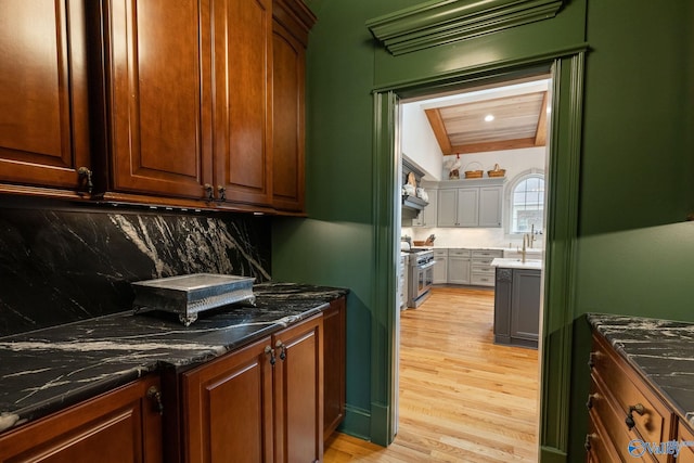 kitchen featuring stainless steel stove, decorative backsplash, light wood-type flooring, and dark stone countertops