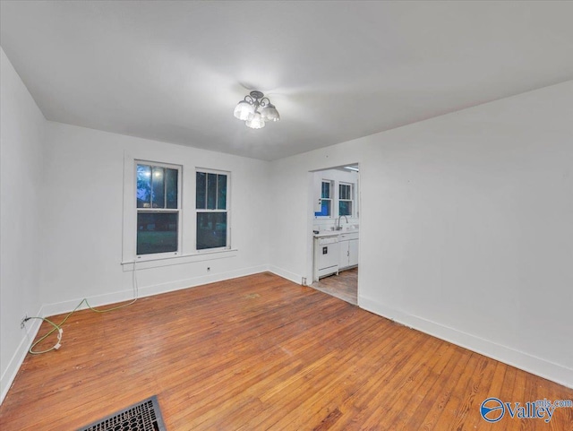 unfurnished room featuring baseboards, wood finished floors, and a sink
