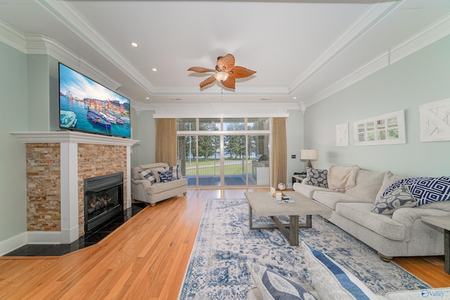 living room with a fireplace, hardwood / wood-style flooring, ornamental molding, ceiling fan, and a raised ceiling