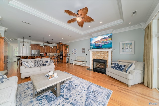 living room with crown molding, ceiling fan, a tray ceiling, a fireplace, and light hardwood / wood-style floors