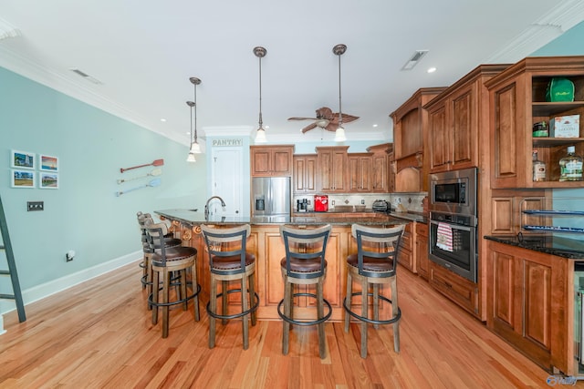 kitchen featuring a breakfast bar, dark stone counters, hanging light fixtures, stainless steel appliances, and a center island with sink