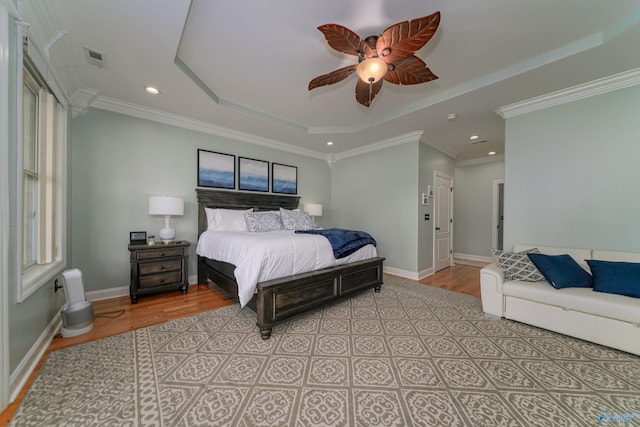 bedroom featuring ceiling fan, ornamental molding, a raised ceiling, and light wood-type flooring