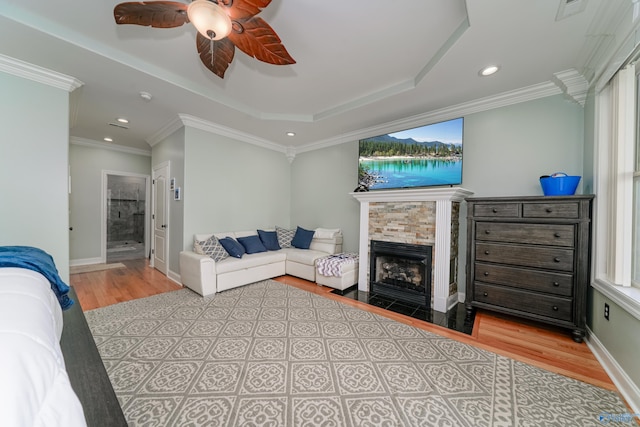 bedroom featuring connected bathroom, ornamental molding, ceiling fan, a tray ceiling, and light wood-type flooring