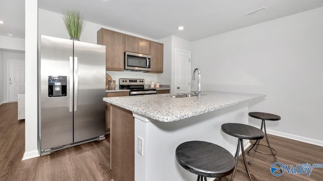 kitchen with a kitchen breakfast bar, a sink, stainless steel appliances, dark wood-style flooring, and visible vents