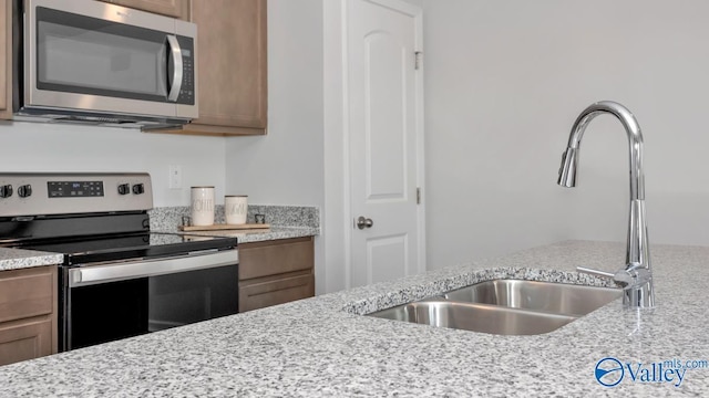 kitchen with brown cabinets, light stone counters, stainless steel appliances, and a sink