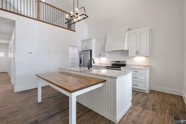 kitchen with premium range hood, decorative light fixtures, appliances with stainless steel finishes, light stone countertops, and white cabinets