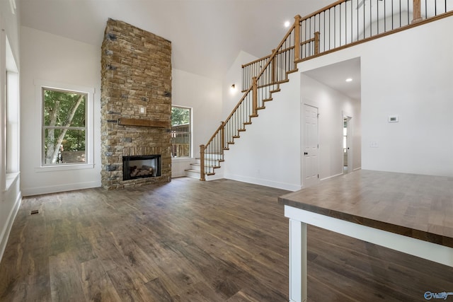 unfurnished living room featuring a towering ceiling, dark hardwood / wood-style floors, and a stone fireplace