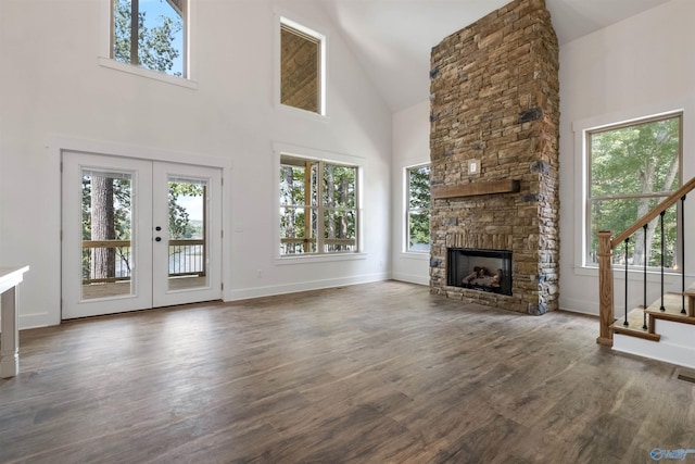 unfurnished living room with a stone fireplace, dark hardwood / wood-style floors, high vaulted ceiling, and french doors