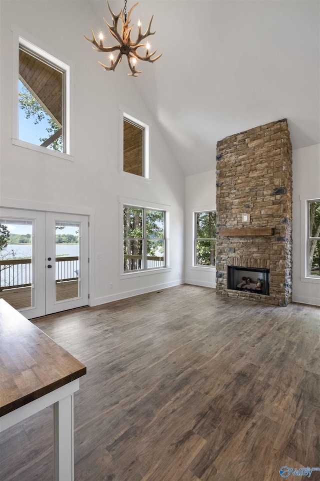 unfurnished living room featuring a stone fireplace, an inviting chandelier, dark hardwood / wood-style flooring, and french doors