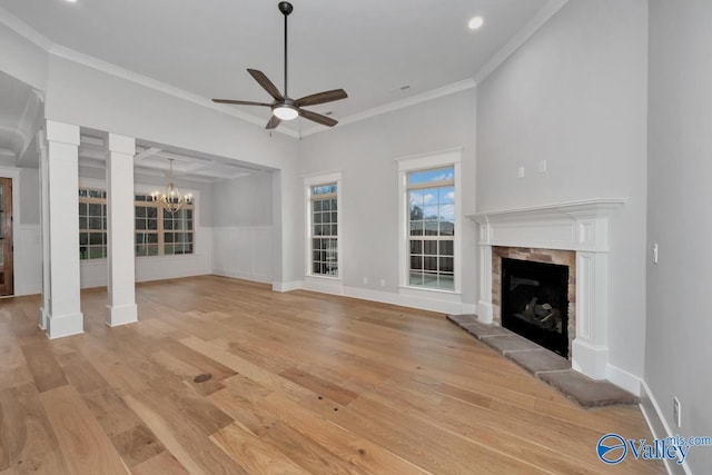 unfurnished living room with ceiling fan with notable chandelier, a stone fireplace, ornamental molding, and light hardwood / wood-style floors