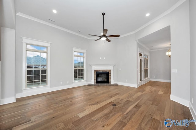 unfurnished living room with a stone fireplace, ceiling fan with notable chandelier, ornamental molding, and wood-type flooring