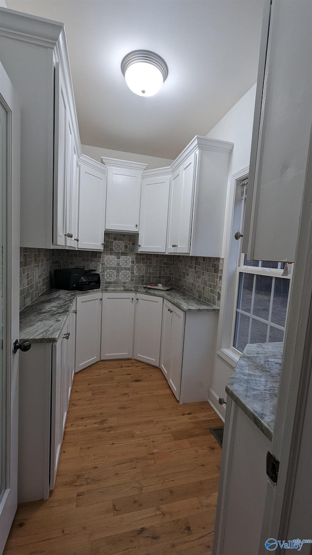 kitchen with stone counters, white cabinetry, backsplash, and light hardwood / wood-style flooring