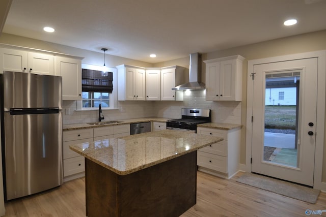 kitchen with pendant lighting, wall chimney range hood, sink, appliances with stainless steel finishes, and light hardwood / wood-style floors