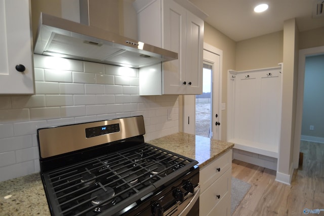 kitchen featuring gas stove, white cabinetry, wall chimney exhaust hood, and light stone countertops