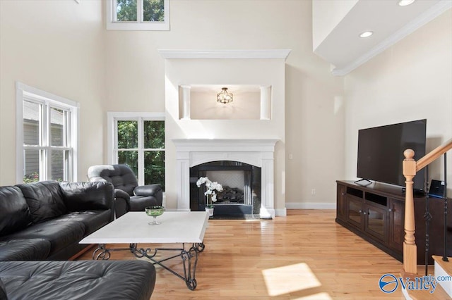 living room with a wealth of natural light, a towering ceiling, light hardwood / wood-style floors, and crown molding