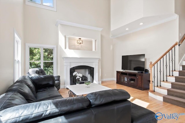 living room with light hardwood / wood-style flooring, a towering ceiling, plenty of natural light, and crown molding