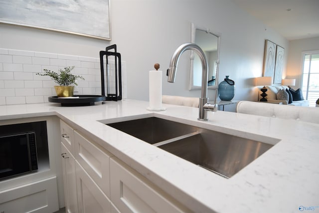 room details featuring white cabinetry, backsplash, light stone countertops, and sink