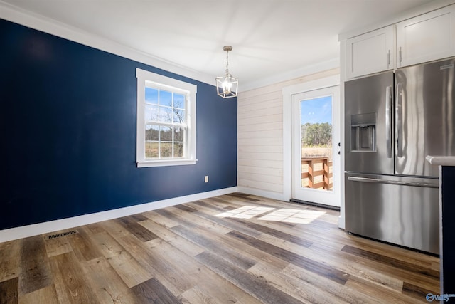unfurnished dining area with a chandelier, baseboards, light wood finished floors, and visible vents