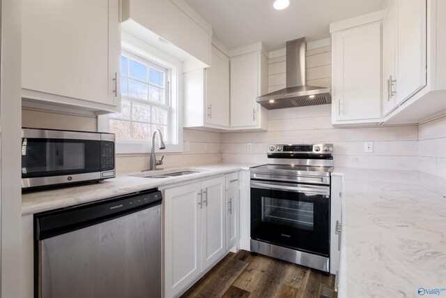 kitchen with stainless steel appliances, dark wood-type flooring, white cabinetry, a sink, and wall chimney range hood