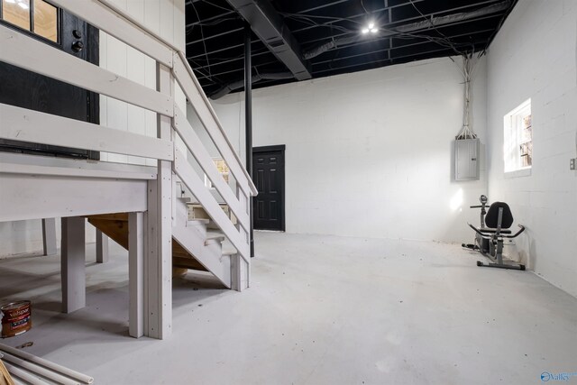 basement with stairs, concrete block wall, and electric panel