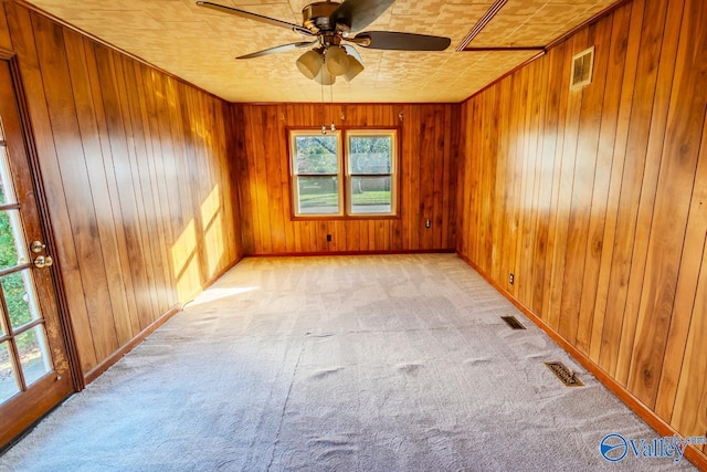 carpeted spare room featuring wooden walls and ceiling fan