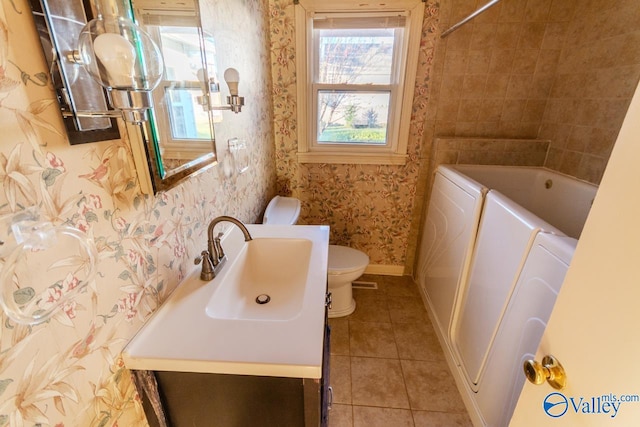 bathroom featuring a washtub, separate washer and dryer, tile patterned flooring, toilet, and vanity