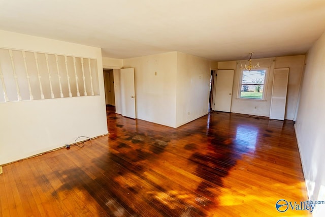 empty room with dark wood-type flooring and a chandelier