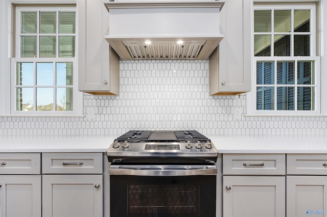 kitchen with backsplash, gas stove, white cabinets, and premium range hood