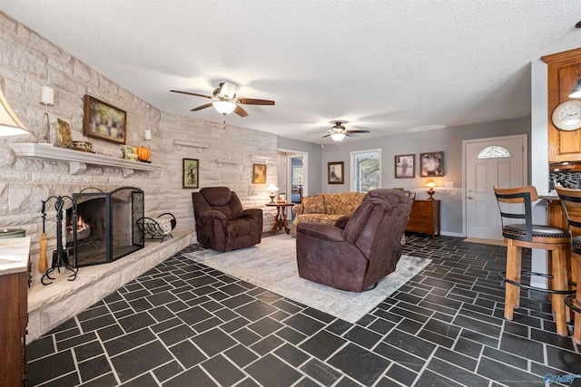 living room featuring a stone fireplace, a textured ceiling, and ceiling fan