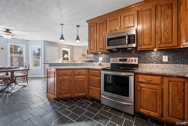 kitchen with light stone counters, appliances with stainless steel finishes, a textured ceiling, hanging light fixtures, and decorative backsplash