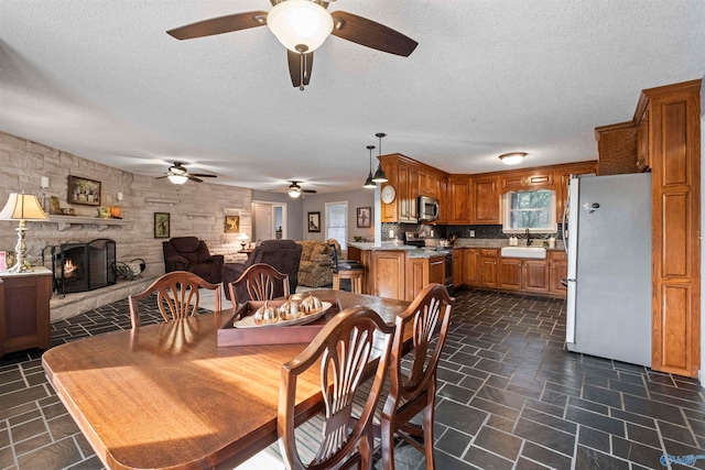 dining area featuring a textured ceiling, sink, ceiling fan, and a fireplace